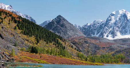 Panorama of Lake Shavlinskoye with a stone mountain similar to a pyramid against the background of rocks with tongues, glaciers and snow in Altai in the sun during the day.