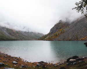 Rain on the alpine turquoise lake Shavlinskoe among the stone rocks with haze of fog and raindrops in Altai.