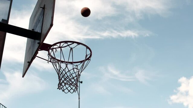 Dark skinned man dunking a basketball against a blue sky.