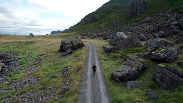 Tourist walking alone between rocks on a lonely gravel road, Aerial Forwarding shot