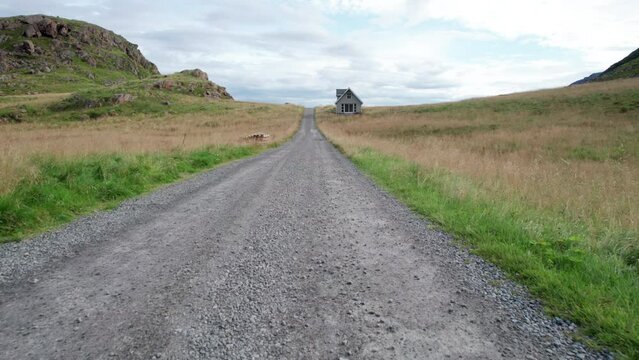Aerial low angle forwarding shot of a one way gravel road with a lonely house on a field of grass