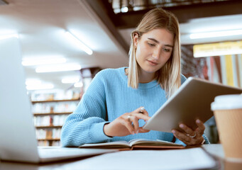 Education, university and woman in library with tablet, research and books for school project or exam. Laptop, notebook and internet, college student studying with technology and elearning on campus.