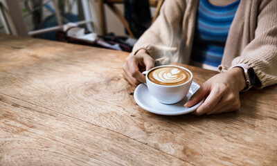 Woman holding a cup of hot latte coffee on the wooden table. morning drink concept