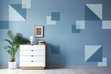 Chest of drawers and houseplant near blue wall in room