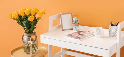 White table and vase with yellow roses near orange wall in room