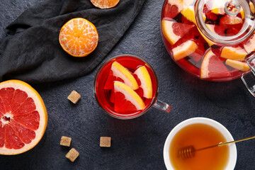 Obraz na płótnie Canvas Glass cup of fruit tea with grapefruit, mandarin, teapot and napkin on dark background