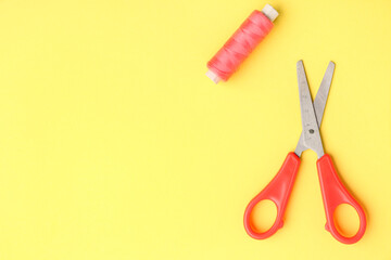 Scissors and thread spool on color background