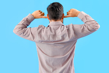 Young man suffering from loud noise on blue background, back view
