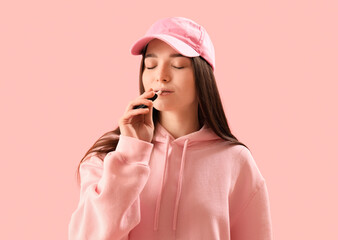 Young woman in cap with disposable electronic cigarette on pink background, closeup