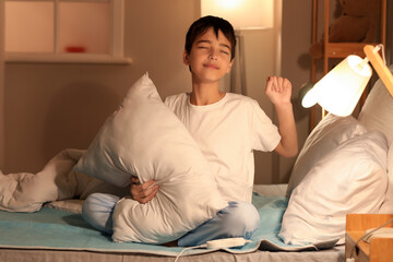 Fototapeta premium Sleepy little boy with pillow sitting on electric heating pad in bedroom at night