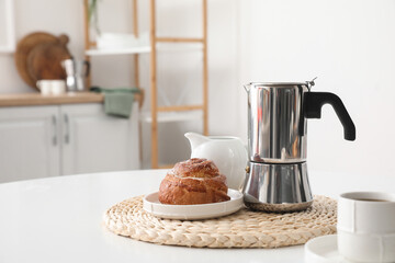 Geyser coffee maker with delicious bun and cup of espresso on table in kitchen
