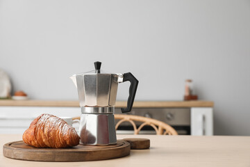 Board with geyser coffee maker and croissant on table in kitchen