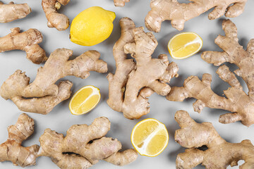 Fresh ginger roots and lemon on grey background, closeup