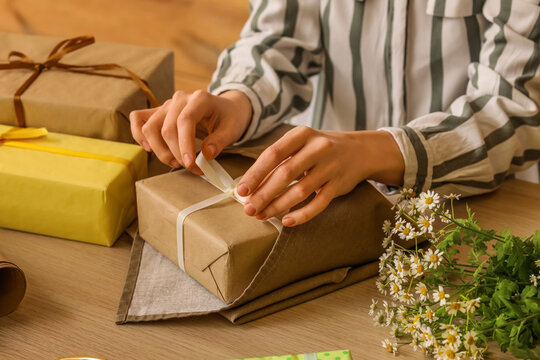 Woman wrapping gift box for International Women's Day at wooden table, closeup