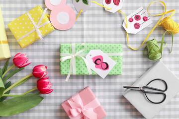 Gift boxes with paper tags and tulips for International Women's Day on checkered fabric background