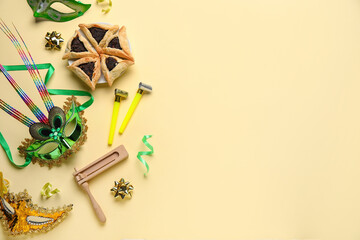 Hamantaschen cookies, carnival masks and noise makers for Purim holiday on yellow background