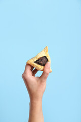 Woman with Hamantaschen cookie for Purim holiday on blue background