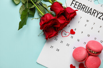 Tasty macaroons, rose flowers and calendar with date 14 FEBRUARY on blue background. Valentine's Day celebration