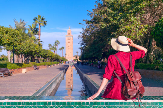 Young woman dressing in red with hat looking  the mosque of Kutubiyyain in Marrakesh