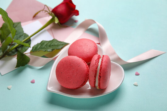 Tasty macaroons, rose flower and envelopes on blue background. Valentine's Day celebration