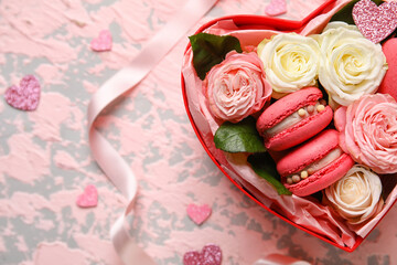 Box with tasty macaroons and rose flowers on pink grunge background. Valentine's Day celebration