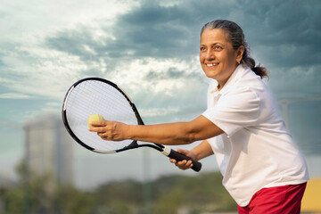 Active senior woman playing tennis on court.