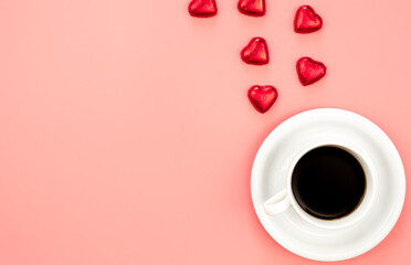 Cup of coffee and heart shaped sweets on a pink background, flat lay.
