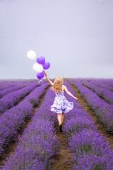 young woman in a lilac dress runs through a field with lavender. She has balloons in her hands