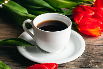 Cup of coffee and red tulips on a wooden surface.