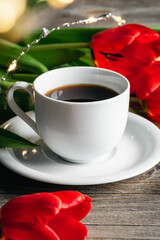 Cup of coffee and red tulips on a wooden surface.
