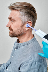 Doctor filling patient's ear canal with silicone material using syringe to make earmolds at hearing...