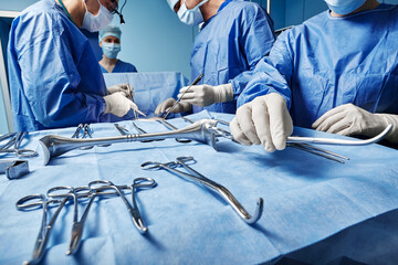 Surgical Team. Surgical nurse giving surgical scissors to male surgeon during operation in operating theatre - obrazy, fototapety, plakaty