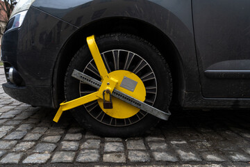 Car wheel blocked by a yellow metal lock or clamp. Vehicle illegal parking violation in a...