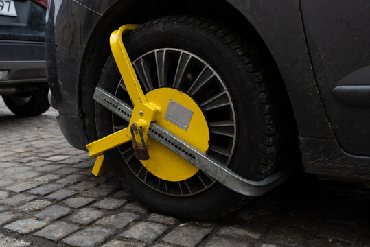 Car wheel blocked by a yellow metal lock or clamp. Vehicle illegal parking violation in a restricted zone.