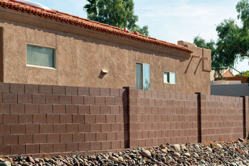 Back yard wall with red bricks and rock garden near sidewalk with orange stucco cement house with...