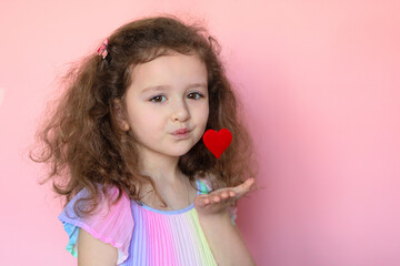Portrait little cute girl send, blowing a kiss heart on pink background. creative child and valentines day. Love concept. copy space, text