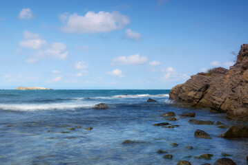 rocky coast at the black sea. calm summer scenery in warm afternoon light. island in the distance beneath a sky with fluffy clouds