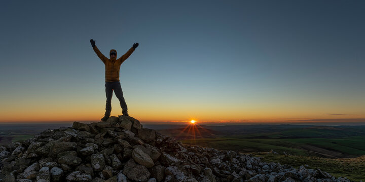 Man with arms raised standing on peak, Preseli Hills, Pembrokeshire, Wales
