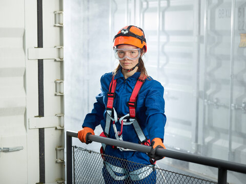 Female worker in climbing harness standing by cargo container, portrait