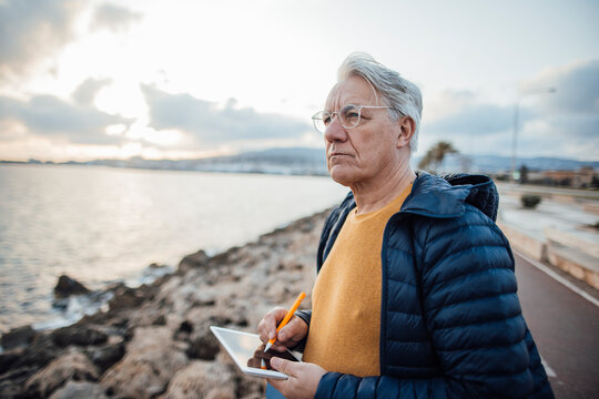 Senior man standing with tablet PC in front of sea at promenade