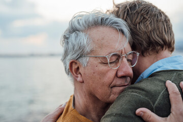 Smiling senior man with gray hair hugging son