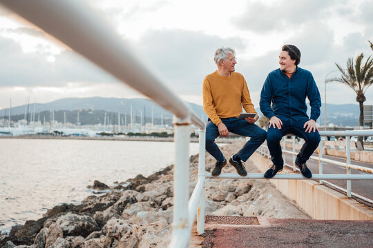 Father and son sitting on railing under cloudy sky
