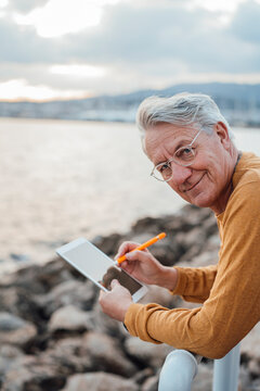 Smiling senior man with tablet PC and digitized pen leaning on railing