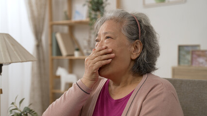shoulder shot of bored asian retired elder woman yawning and wiping tears from eyes while staying at home alone in the living room during the day.