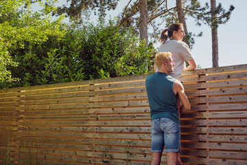 Happy man carrying woman looking over wooden fence at back yard