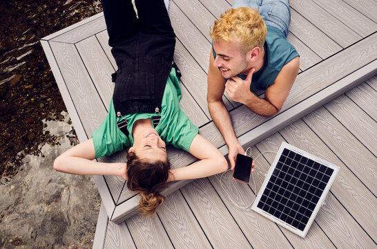 Smiling couple relaxing on patio with smart phone getting charged by solar panel