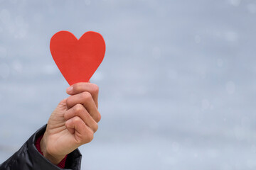 Valentine's Day card with a heart.A woman's hand holds a red paper heart on a light background.