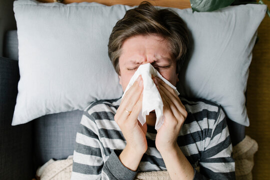 Man blowing nose in napkin lying on bed
