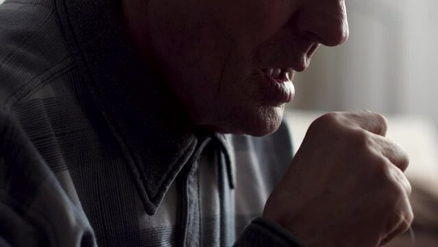Caucasian pensioner coughing into his fist while at home. selective focus.illness and cough, asthmatic elderly man, throat disease in an old man.Coronavirus in pensioners