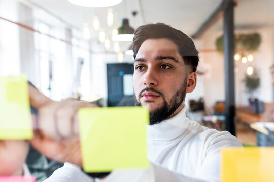 Young Businessman Sticking Adhesives Notes On Glass